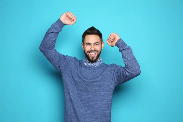 Happy young man celebrating victory on color background