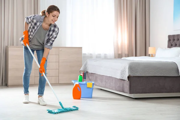 Young woman washing floor with mop in bedroom. Cleaning service