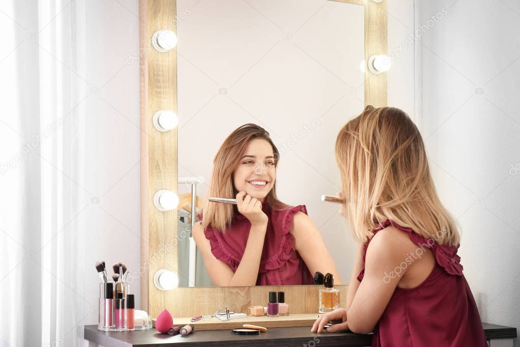 Woman applying makeup near mirror with light bulbs in dressing room
