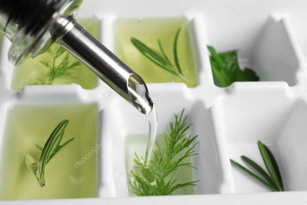 Pouring oil into ice cube tray with herbs, closeup