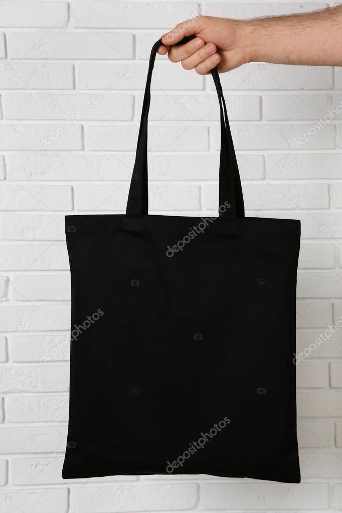 Man holding cotton shopping eco bag against brick wall. Mockup for design