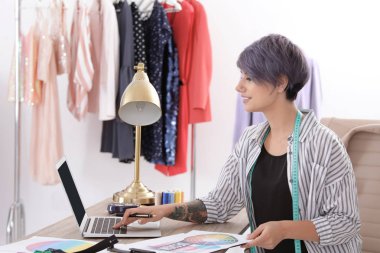 Güzel genç stilist Studio dizüstü bilgisayar ile çalışma. Moda giysiler