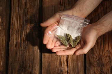 Plastik torba kokain ve kenevir tomurcukları ahşap arka plan, closeup üzerinde tutan adam. Metin için yer