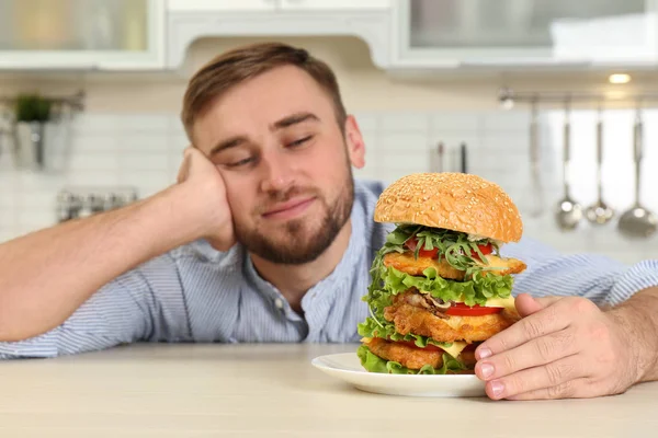 Young hungry man and huge burger on table