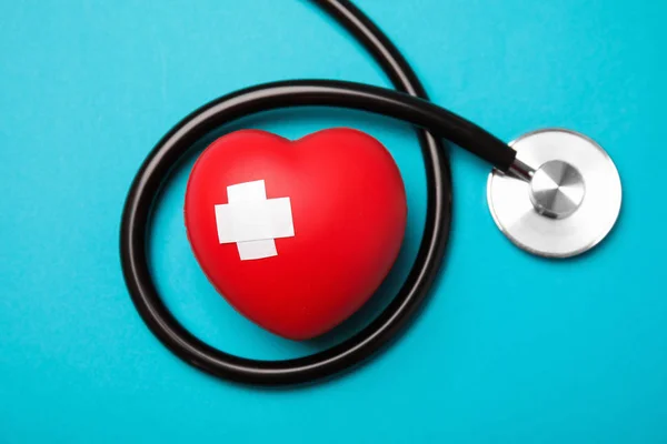 Stethoscope and red heart with adhesive plasters on color background, top view. Cardiology concept