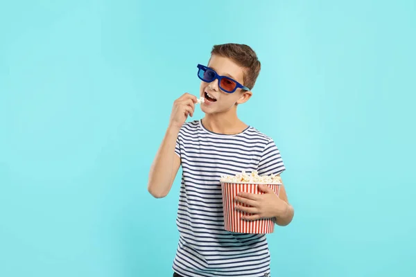 Boy with 3D glasses and popcorn during cinema show on color background
