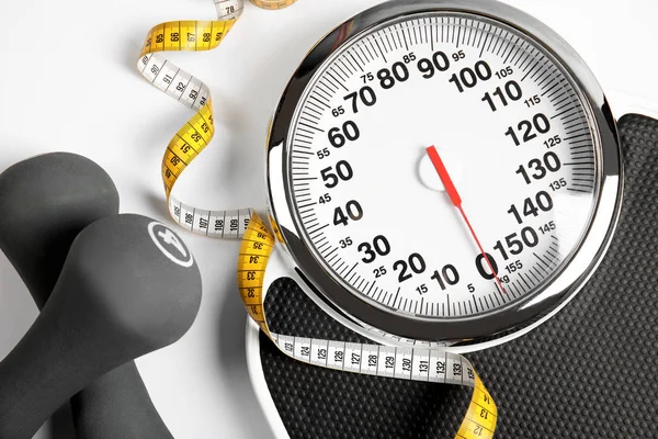 Modern scales, tape measure and dumbbells on white background