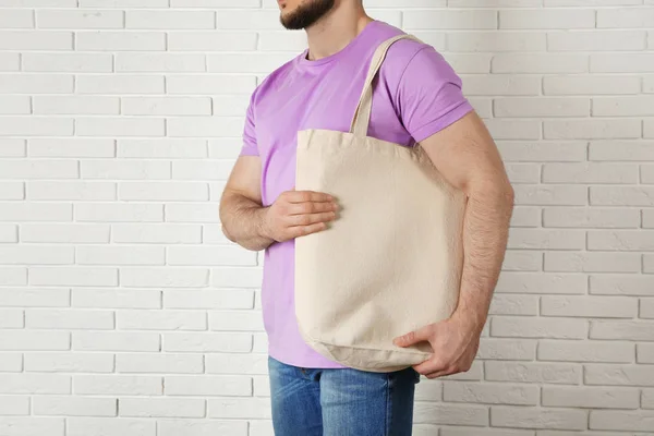 Man with cotton shopping eco bag against brick wall. Mockup for design