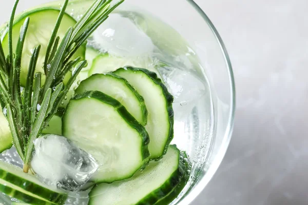 Glass of fresh cucumber water on light background, top view