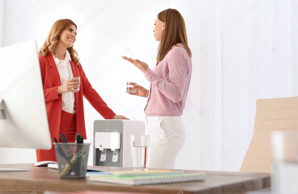 Women having break near water cooler at workplace