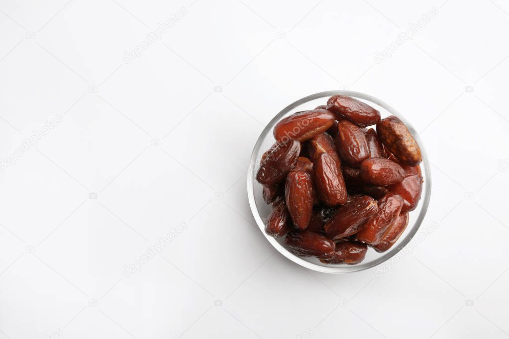 Bowl with sweet dried date fruits on white background, top view. Space for text