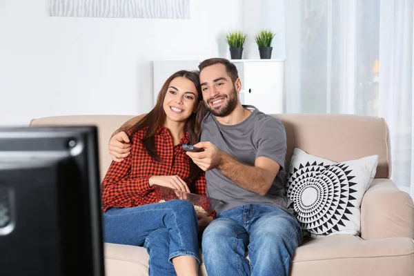 Happy young couple watching TV on sofa at home