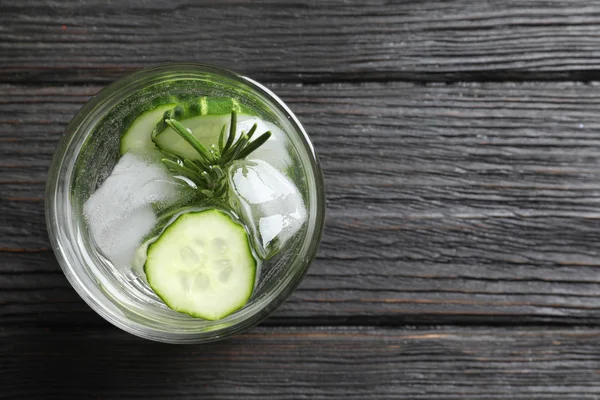 Glass of fresh cucumber water on wooden table, top view. Space for text