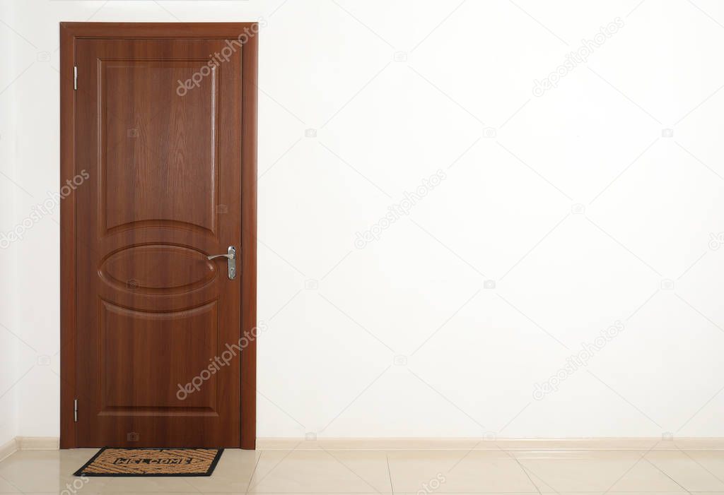 Closed brown door with welcome mat in white wall. Space for text