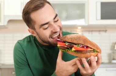 Genç aç adam mutfakta lezzetli sandviç yeme
