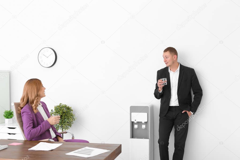 Office employee with glass near water cooler at workplace, closeup. Space for text