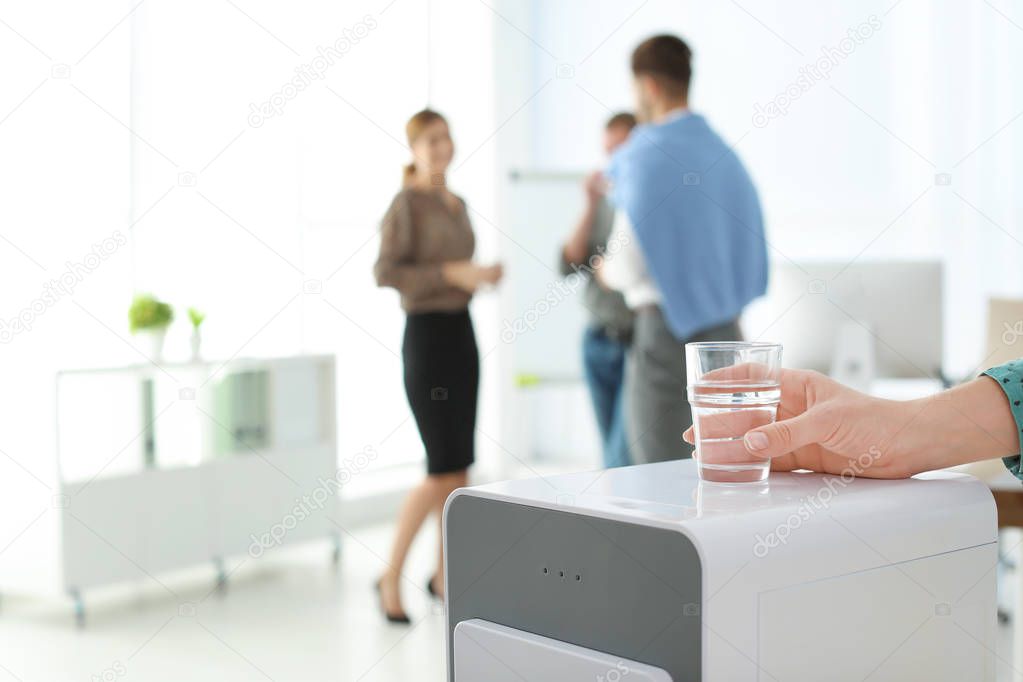 Office employee with glass near water cooler at workplace, closeup. Space for text