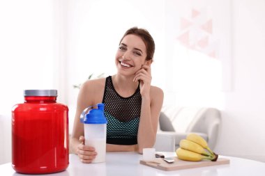 Odada protein shake malzemelerle masada şişe tutan genç kadın