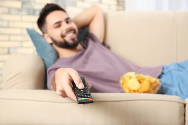 Uzaktan Kumanda Tv izlerken koltukta evde, odak üstünde el ile genç adam