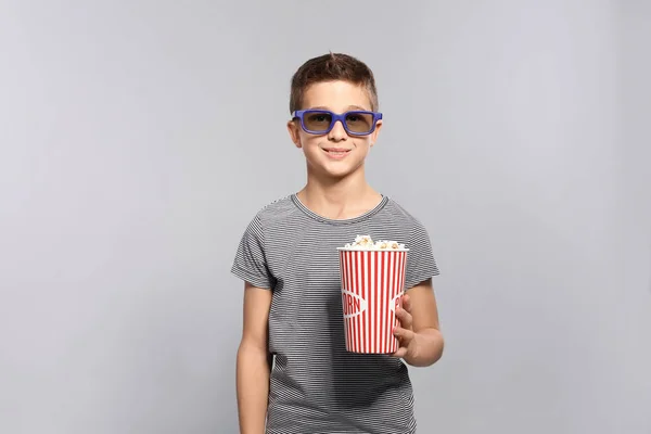 Boy with 3D glasses and popcorn during cinema show on grey background