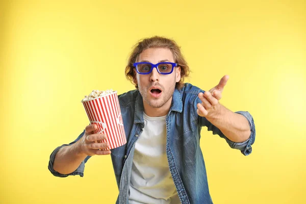 Emotional man with 3D glasses and popcorn during cinema show on color background