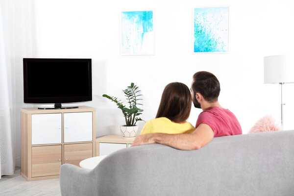 Young couple watching TV on sofa at home