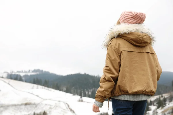 年轻女子穿着暖和的衣服在雪山附近 空间为文字 — 图库照片