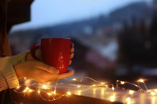 Mulher Segurando Xícara Bebida Quente Varanda Decorada Com Luzes Natal — Fotografia de Stock