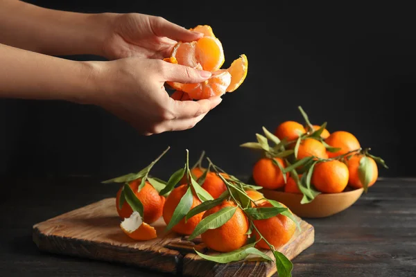 Woman peeling ripe tangerine over table on dark background, closeup