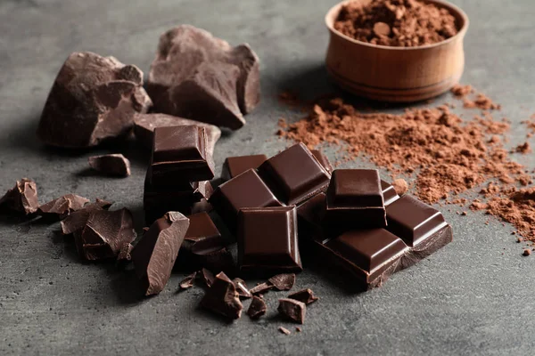 Pieces of chocolate and cocoa powder on grey background