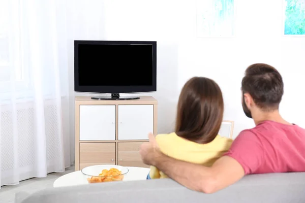年轻的夫妇在家里的沙发上看电视 图库图片