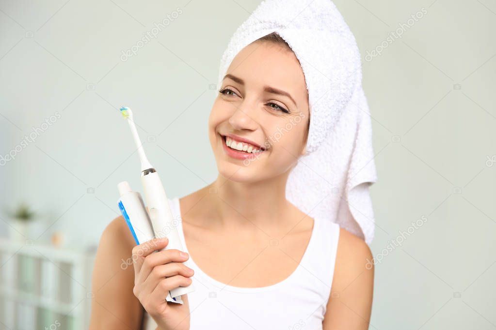 Portrait of young woman with electric toothbrush and paste on blurred background