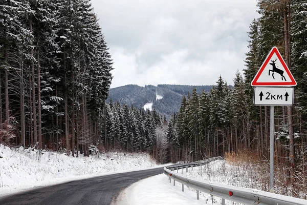 Wild animals warning traffic sign near road with snow on sides through forest