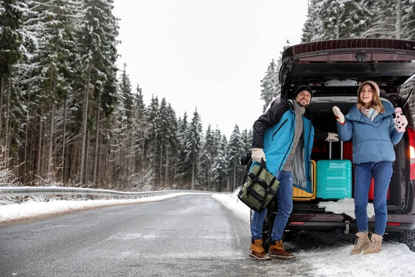 Couple near open car trunk full of luggage on road, space for text. Winter vacation