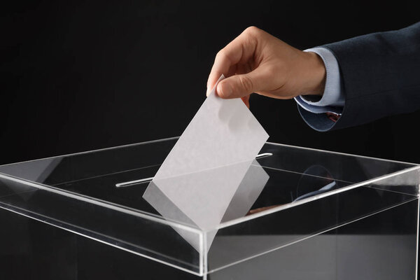 Man putting his vote into ballot box on black background, closeup