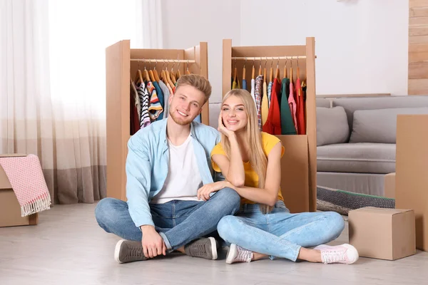 Happy young couple sitting near wardrobe boxes indoors
