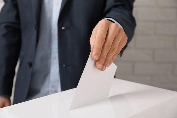 Man putting his vote into ballot box against brick wall, closeup