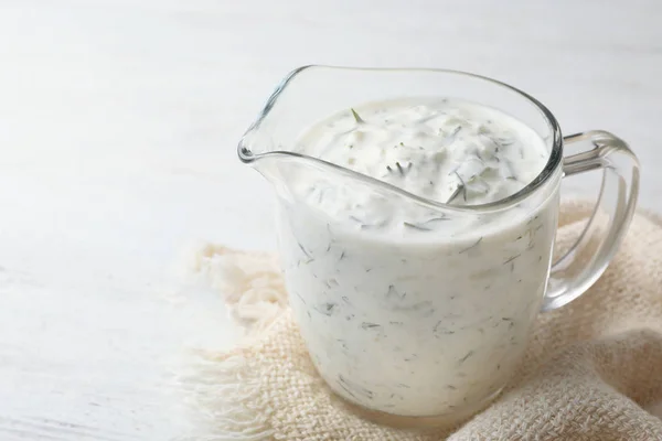 Glass jug of cucumber sauce on wooden background, space for text. Traditional Tzatziki
