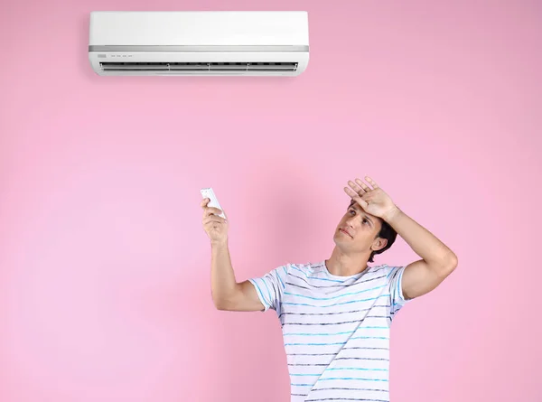 Junger Mann Leidet Unter Hitze Und Schaltet Klimaanlage Vor Farbigem — Stockfoto