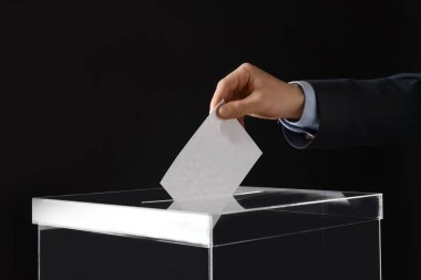 Man putting his vote into ballot box on black background, closeup clipart