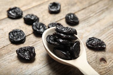 Spoon of dried plums on wooden background, closeup. Healthy fruit