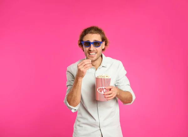 Emotional man with 3D glasses and popcorn during cinema show on color background