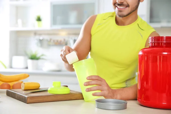 Young man preparing protein shake at table in kitchen, closeup. Space for text