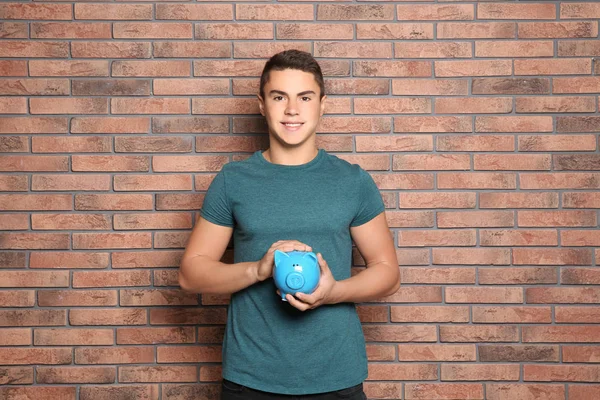 Teenage boy with piggy bank near brick wall