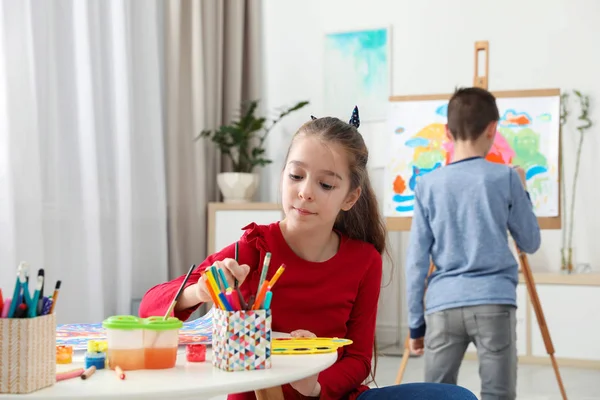 テーブルと室内イーゼルの近くに少年の絵の女の子 創造的な子供 — ストック写真