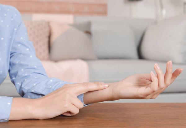 Young woman checking pulse indoors, closeup. Space for text