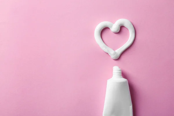 Heart shape made of toothpaste near tube and space for text on color background, top view