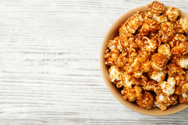 Bowl with caramel popcorn on white wooden background, top view. Space for text