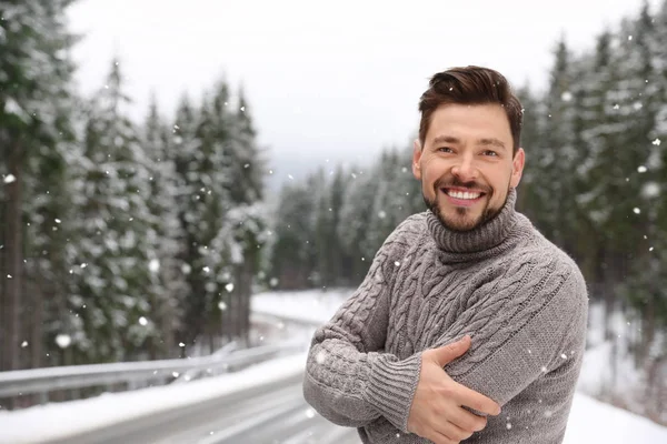Man in warm sweater outdoors on snowy day, space for text. Winter vacation