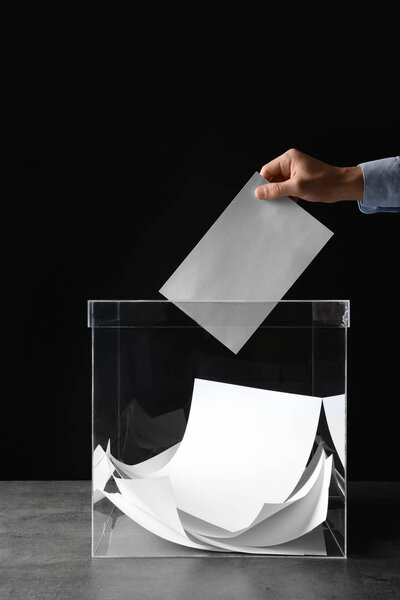 Человек кладет свой голос в урну для голосования на столе на черном фоне, крупным планом
